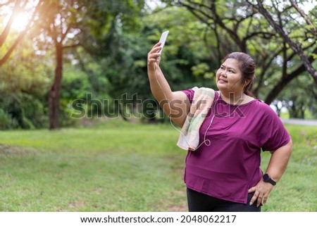 Asian fat woman workout outdoors with use a smartphone to take pictures, Sport and recreation for weight loss idea concept.