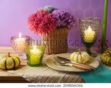 Thanksgiving holiday table decoration with plate, candles and pumpkin over purple background