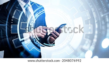 Businessman wearing formal suit is touching smartphone screen with his finger. New York city skyscraper downtown in the background. Digital interface with circle hologram in the foreground