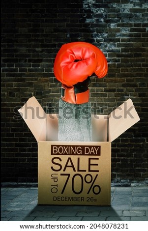Close up of boxing hand coming out from a gift box with text of Boxing Day sale with up to 70% off in bricks wall background