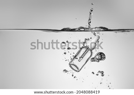 Bottle of essential oil in water on grey background