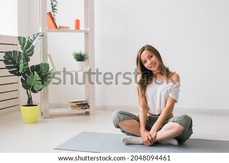 Positive girl sitting on fitness mat resting after pilates or yoga practice. Mindfulness and wellbeing concept.