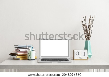 Workspace with modern laptop near light wall in office