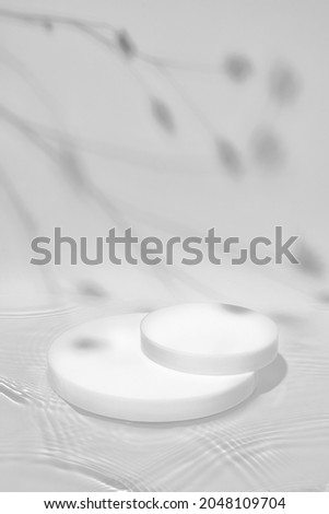 Abstract nature scene with white cylinder podium on transparent water texture with waves, soft shadow of plants on white wall. Pedestal for cosmetic product and packaging mockups display presentation