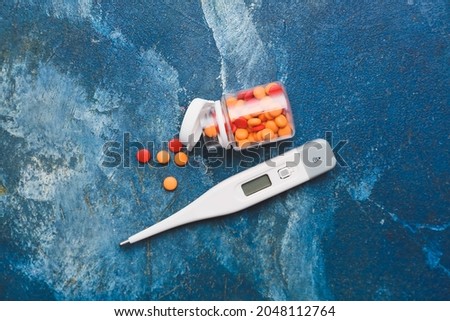 Electronic thermometer with pills on color background