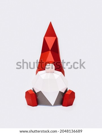 Volumetric paper Christmas gnome in red pointed hat on light , polygonal figure dwarf, Happy New Year and Merry Christmas holiday background with copy space. 