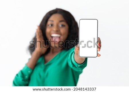 Emotional young black woman showing cellphone with blank screen on white studio background, recommending newest nice mobile application for smartphone, mockup, copy space, closeup photo