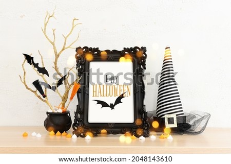 holidays image of Halloween. witcher hat, broom, bare trees, photo frame over white wooden table