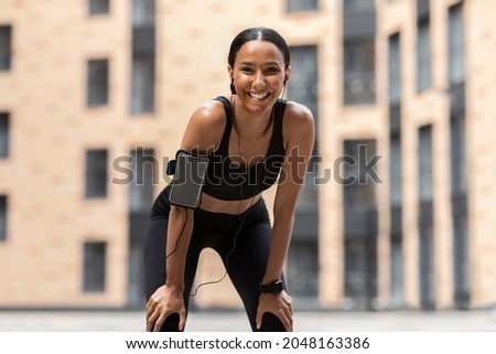 Sporty Young Female Leaning On Knees, Catching Breath After Training Outdoors, Athletic Woman In Stylish Sportswear Relaxing After Stamina Workout, Standing On Urban Street And Smiling At Camera Royalty-Free Stock Photo #2048163386