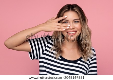 Funny cute blond girl, isolated studio portrait. Happy cheerful female in casual t-shirt with natural makeup and blonde hair posing. Young woman with blue eyes and white nail polish over pink wall