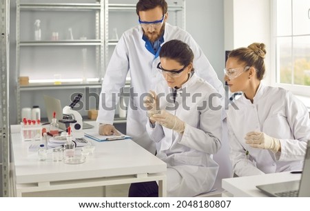 Male and female scientists working in laboratory, doing medical research, developing new vaccine for humans. Serious man and woman looking at chemical sample sitting at table in science lab