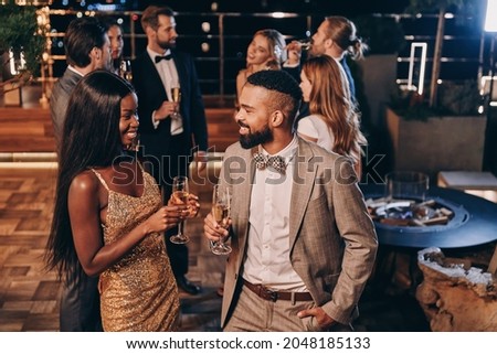 Beautiful young African couple in formalwear holding champagne flutes and smiling Royalty-Free Stock Photo #2048185133
