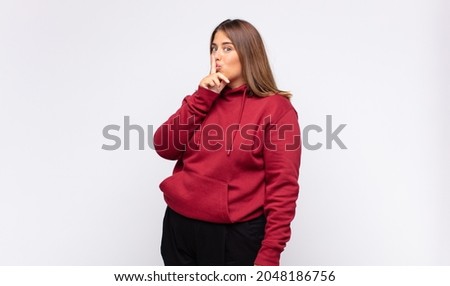 young blonde woman asking for silence and quiet, gesturing with finger in front of mouth, saying shh or keeping a secret