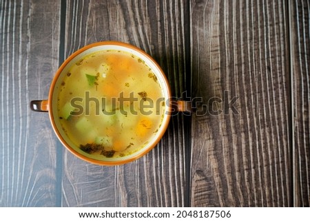 chicken broth with vegetables and zucchini in a brown plate lies on a wooden table. top view. homemade food