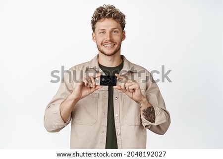 Young smiling caucasian man showing his credit discount card and looking happy, recommending bank, standing over white background
