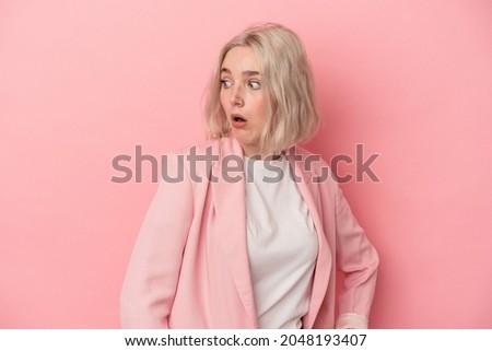Young caucasian woman isolated on pink background looks aside smiling, cheerful and pleasant.