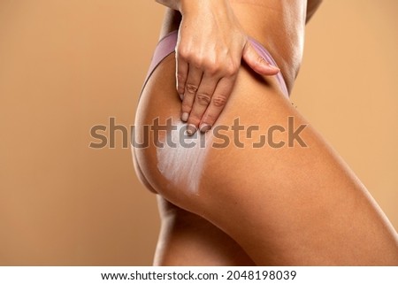 woman applying stretch marks cream on her bottom on a beige background