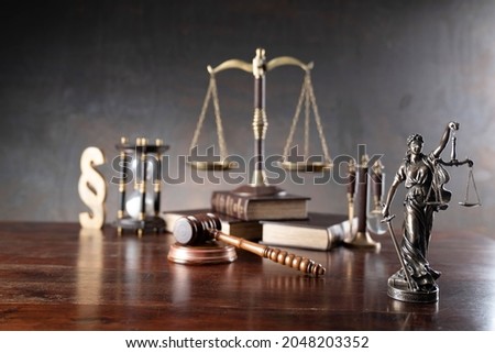 Attorney at law concept. Judges gavel, wooden desk, statue of justice, paragraph symbol, hourglass, books,  dark background.