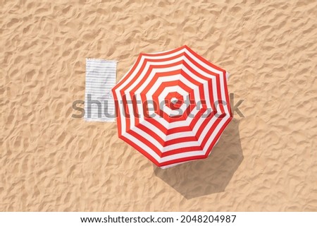 Striped beach umbrella near towel on sand, aerial view Royalty-Free Stock Photo #2048204987