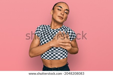 Hispanic transgender man wearing make up and long hair wearing modern clothes smiling with hands on chest with closed eyes and grateful gesture on face. health concept. 