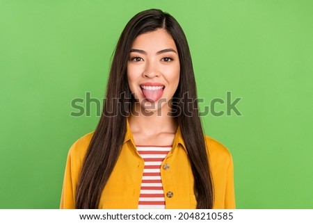 Photo of cute tricky young woman dressed casual clothes showing tongue isolated green color background