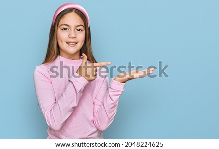 Beautiful brunette little girl wearing casual turtleneck sweater amazed and smiling to the camera while presenting with hand and pointing with finger. 