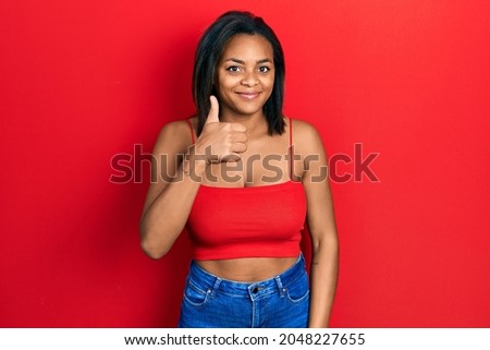 Young african american girl wearing casual style with sleeveless shirt doing happy thumbs up gesture with hand. approving expression looking at the camera showing success. 