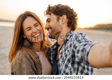 White young couple laughing and hugging while taking selfie photo outdoors