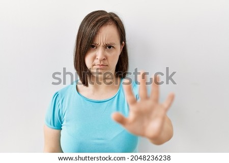 Young down syndrome woman standing over isolated background doing stop sing with palm of the hand. warning expression with negative and serious gesture on the face. 