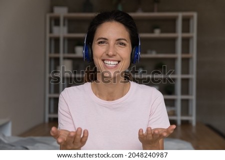 Close up headshot portrait of smiling young Caucasian woman in headphones speak talk on video call at home. Profile picture of happy millennial female in earphones have webcam virtual event.
