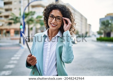 Young hispanic business woman wearing professional look smiling confident at the city holding worker clipboard Royalty-Free Stock Photo #2048242964