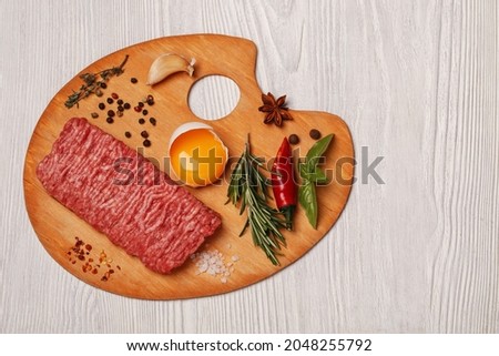 Culinary art  concept - ground meat, egg, pepper, basil, rosemary, spices on palette artist above picture frame. 