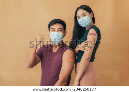 Asian man and woman showing shoulders after getting a vaccine. Happy couple showing arm with band-aids on after vaccine injection. Royalty-Free Stock Photo #2048258177