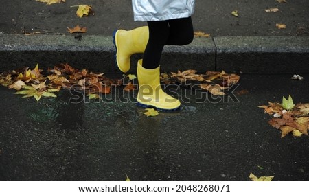 Yellow rubber shoes in puddle after raining. Falling leaves. Autumn season concept.	