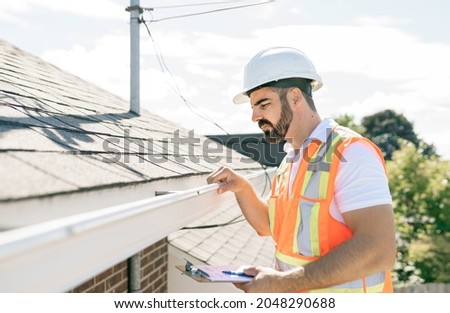 A man in a hard hat, holding a clipboard, standing on the steps of an old rundown house. Royalty-Free Stock Photo #2048290688