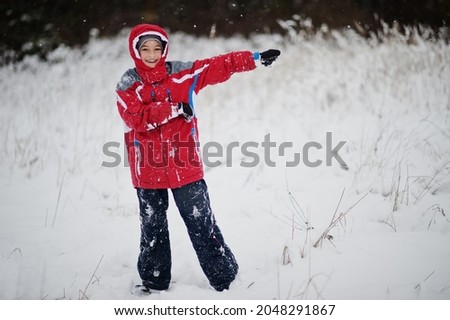 Happy boy wear red jacket at winter day. Walking in the park on cold day with snow.