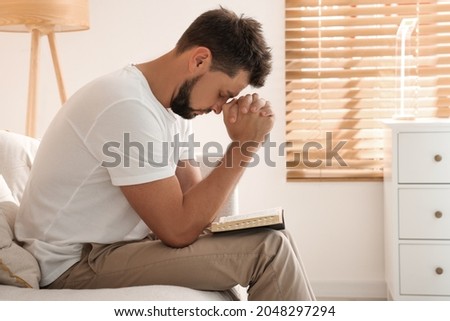 Religious man with Bible praying indoors. Space for text