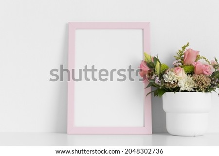 Pink frame mockup with a bouquet of roses on the white table.