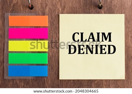 yellow card with the text CLAIM DENIED on a wooden background next to colored stickers