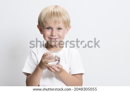 Handsome Caucasian child, blond boy with glass of water. White studio background. Concept of clean water that can be drunk by children, world problem of water resources and drinking water. Copy space