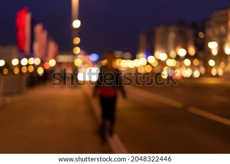 Soft focus blurred image silhouette of a woman walking along the road at night.