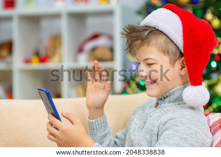A boy in a Santa hat at home on the couch calls his relatives via the Internet to wish them a Merry Christmas (New Year)