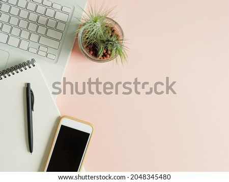 Smartphone, white blank notebook paper, black pen, laptop blank keyboard and indoor plant pot flat lay on pastel pink background. Lifestyle theme background (top view, selective focus, space for text)