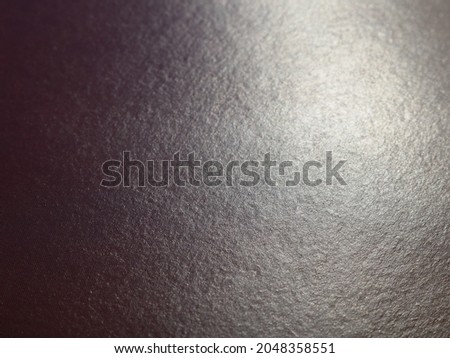 dark textured glossy background with a light spot, black sheet of paper reflecting bright light, dark paper texture illuminated from one edge Royalty-Free Stock Photo #2048358551