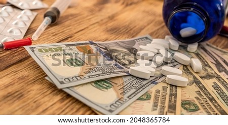on a wooden table are American dollar bills on which are poured white pills from a bottle. Medicine concept