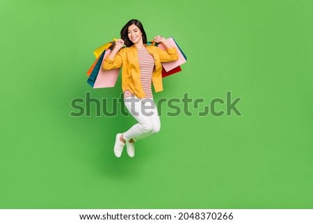 Full body photo of cool brown hairdo millennial lady hold bags jump wear shirt trousers sneakers isolated on green color background