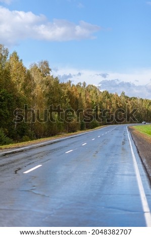 Straight road with a marking on the nature background. Open Road in future, no cars, auto on asphalt road through green forest, trees. Clouds on blue sky in summer, sunshine, sunny day. Bottom view