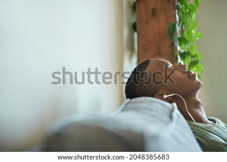 Young African man relaxing to music on earphones on his sofa