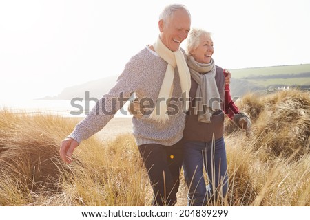 Senior Couple Walking Through Sand Dunes On Winter Beach Royalty-Free Stock Photo #204839299