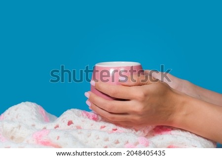 Close-up view stock color photography of manicured female hands holding cute pink mug isolated on blue wall background